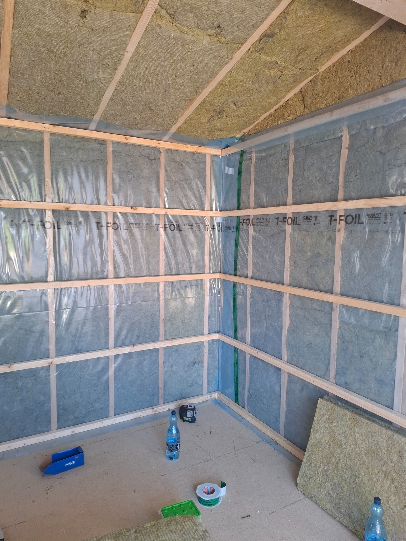 Wnętrze konstrukcji szkieletowej z izolacją z wełny mineralnej, zabezpieczonej folią. Widoczne drewniane elementy konstrukcyjne i narzędzia pracy.