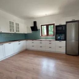 Nowoczesna kuchnia z białymi frontami szafek, drewnianym blatem i turkusowymi płytkami na ścianie, z widocznym oknem i sprzętem AGD.