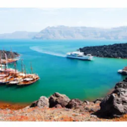 Panoramiczny widok na Santorini: białe domy na klifie, błękitne morze, statki na tle wulkanicznej wyspy i charakterystyczne kopuły.