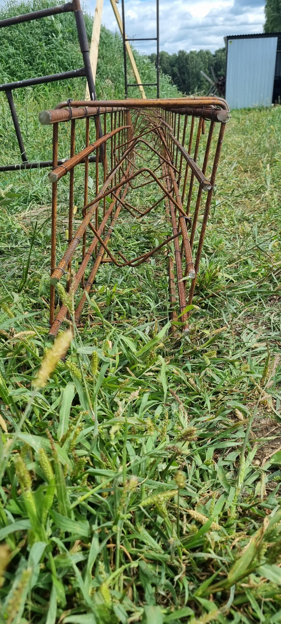 Zbrojenie z prętów stalowych, ułożone na trawie, przygotowane do wylania fundamentów, widoczne wiązania drutem.