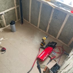 Krystian Gaik - Wnętrze w trakcie ocieplania wełną mineralną, widoczne narzędzia pracy: wiertarka, poziomica, miarka, pudełko gwoździ Hilti, przewody i rury