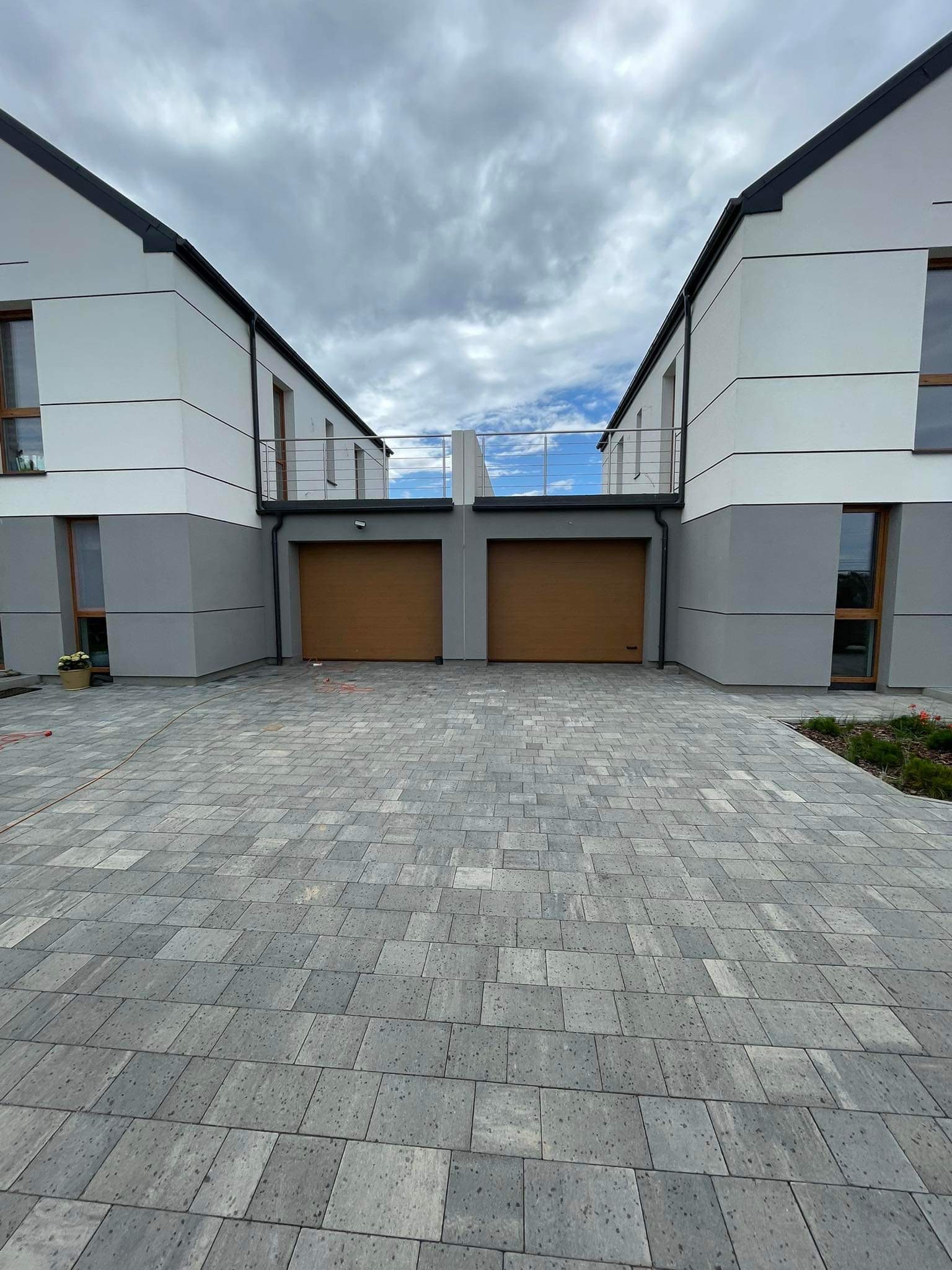 Dwa segmenty bliźniacze z balustradami nierdzewnymi na balkonach i brukowanym podjazdem z szarej kostki.