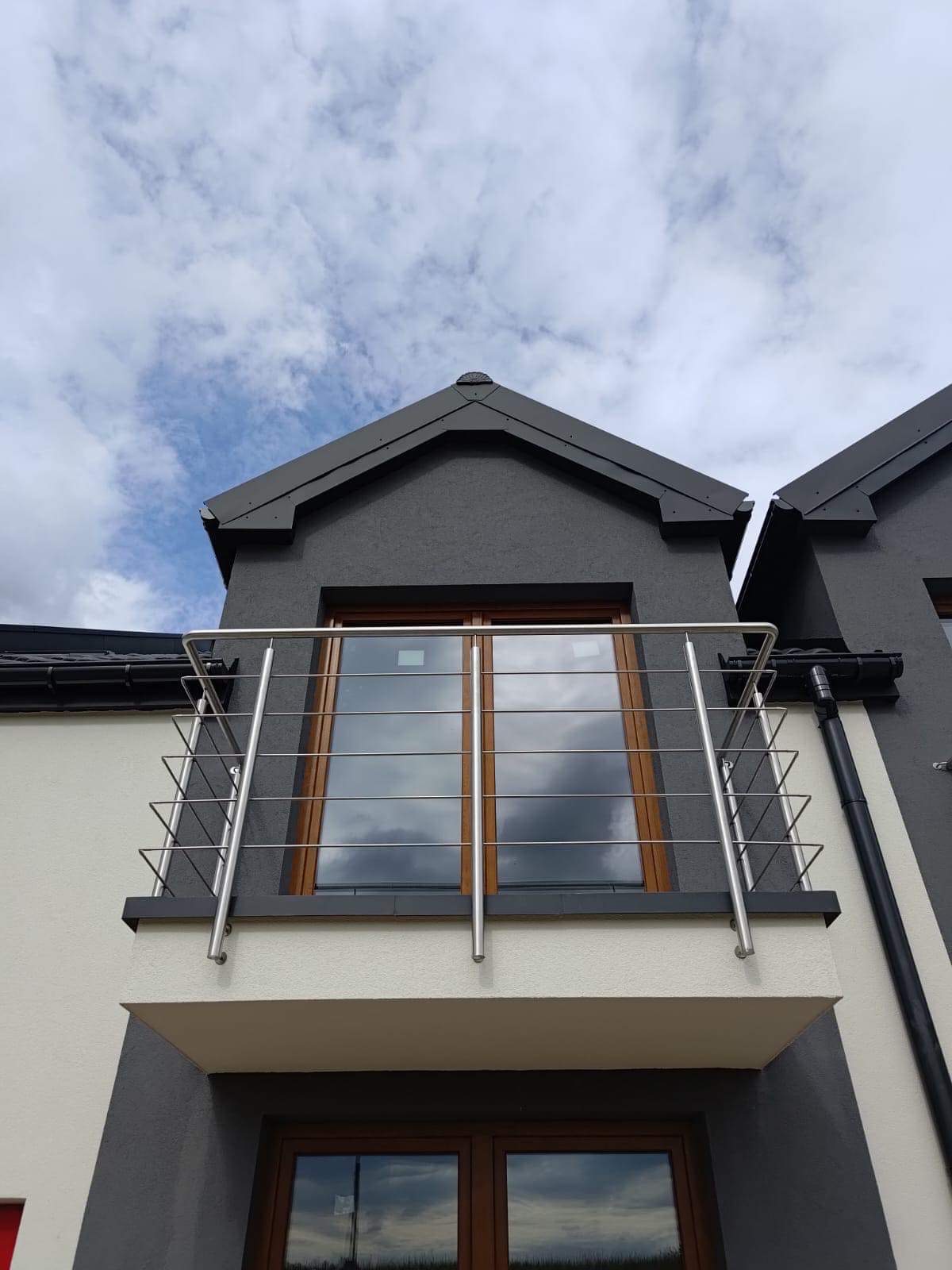 Balkon z nowoczesną balustradą ze stali nierdzewnej z poziomymi linkami, widok z dołu na tle pochmurnego nieba.