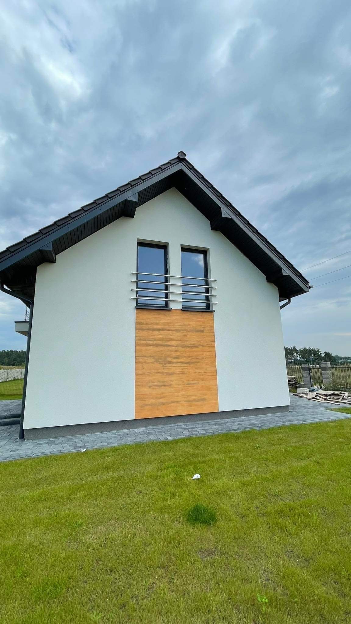 Nowoczesny dom jednorodzinny z białymi ścianami i drewnianą elewacją, z balkonem zabezpieczonym poziomymi, metalowymi barierkami.