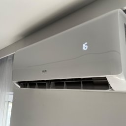 Abm-Klimatyzacja - Biała klimatyzacja marki AUX zamontowana na ścianie, wyświetlająca temperaturę 16 stopni, widoczne zasłony w tle.