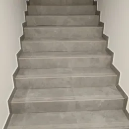 Schody wyłożone szarymi płytkami ceramicznymi z antypoślizgowymi paskami, widok z dołu.