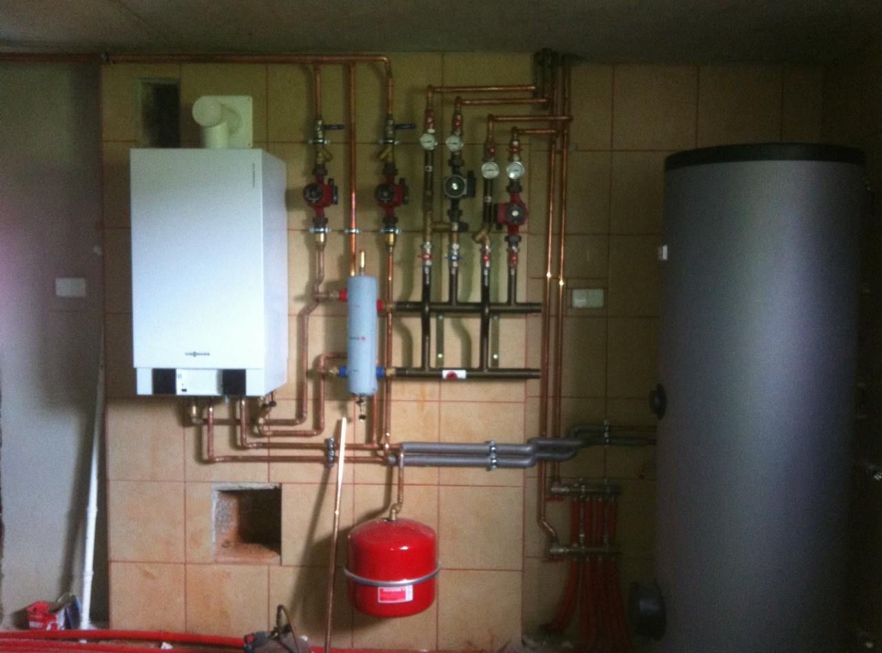 Zamontowany piec gazowy Viessmann z instalacją hydrauliczną, zbiornikiem i miedzianymi rurami na ścianie z beżowych płytek. Widoczne elementy instalacji CO.