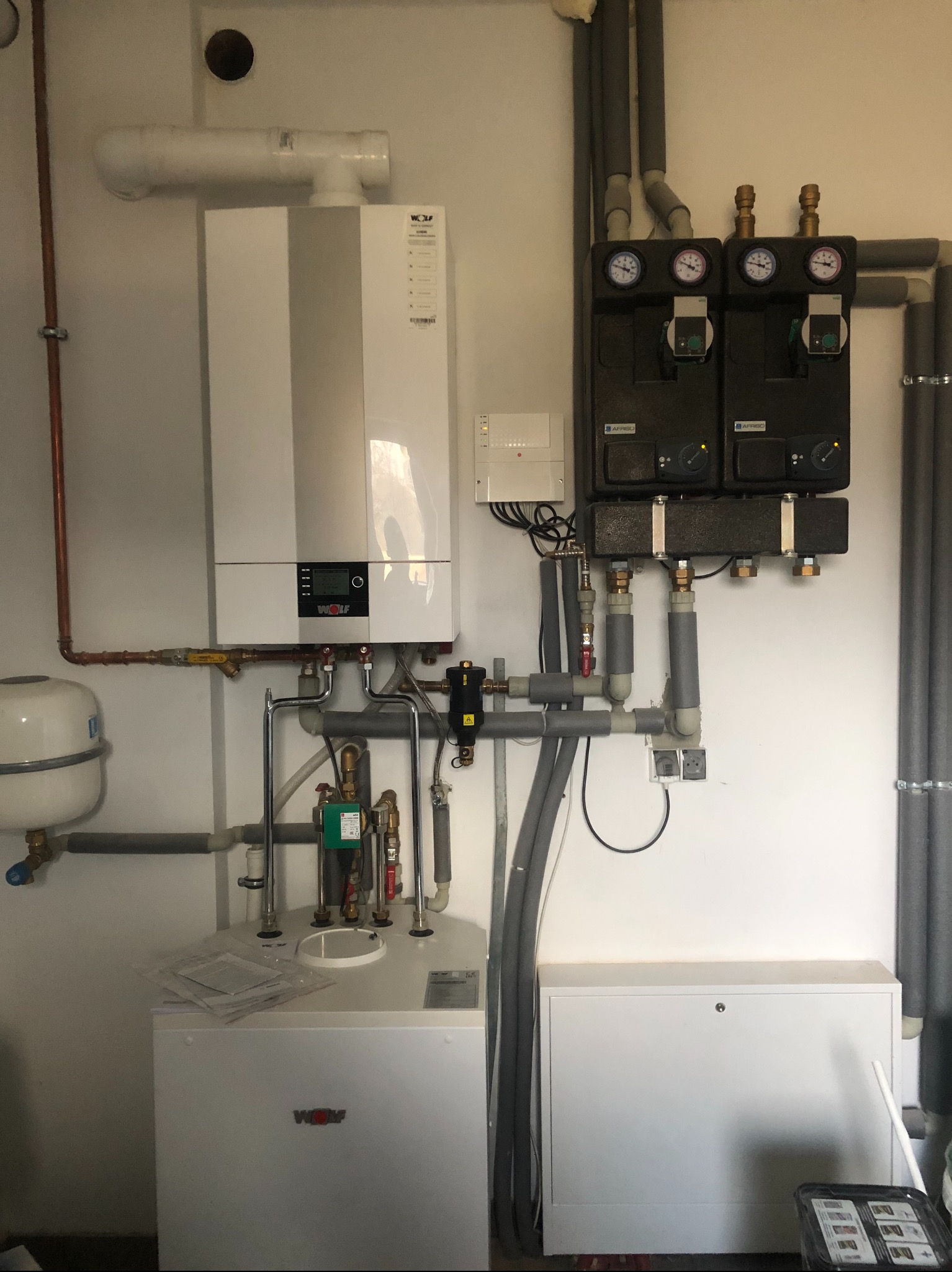 Zainstalowany, biały piec gazowy marki Wolf z podłączonymi rurami miedzianymi i szarymi rurami izolowanymi, manometry Afriso, biała skrzynka z bezpiecznikami, biały zbiornik wyrównawczy...