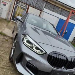 Szary samochód marki BMW, po detailingu, zaparkowany przed budynkiem warsztatu z widocznym szyldem 'Custom Detailing'.