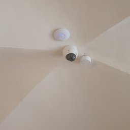 Soundtec - Kamera kopułkowa BCS, punkt dostępowy Wi-Fi z niebieską diodą i czujnik na suficie w jasnym odcieniu beżu.