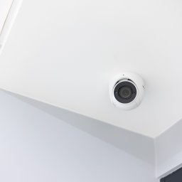 Soundtec - Kamera monitoringu kopułkowa, zamontowana na białym suficie w rogu pomieszczenia, widok z dołu.