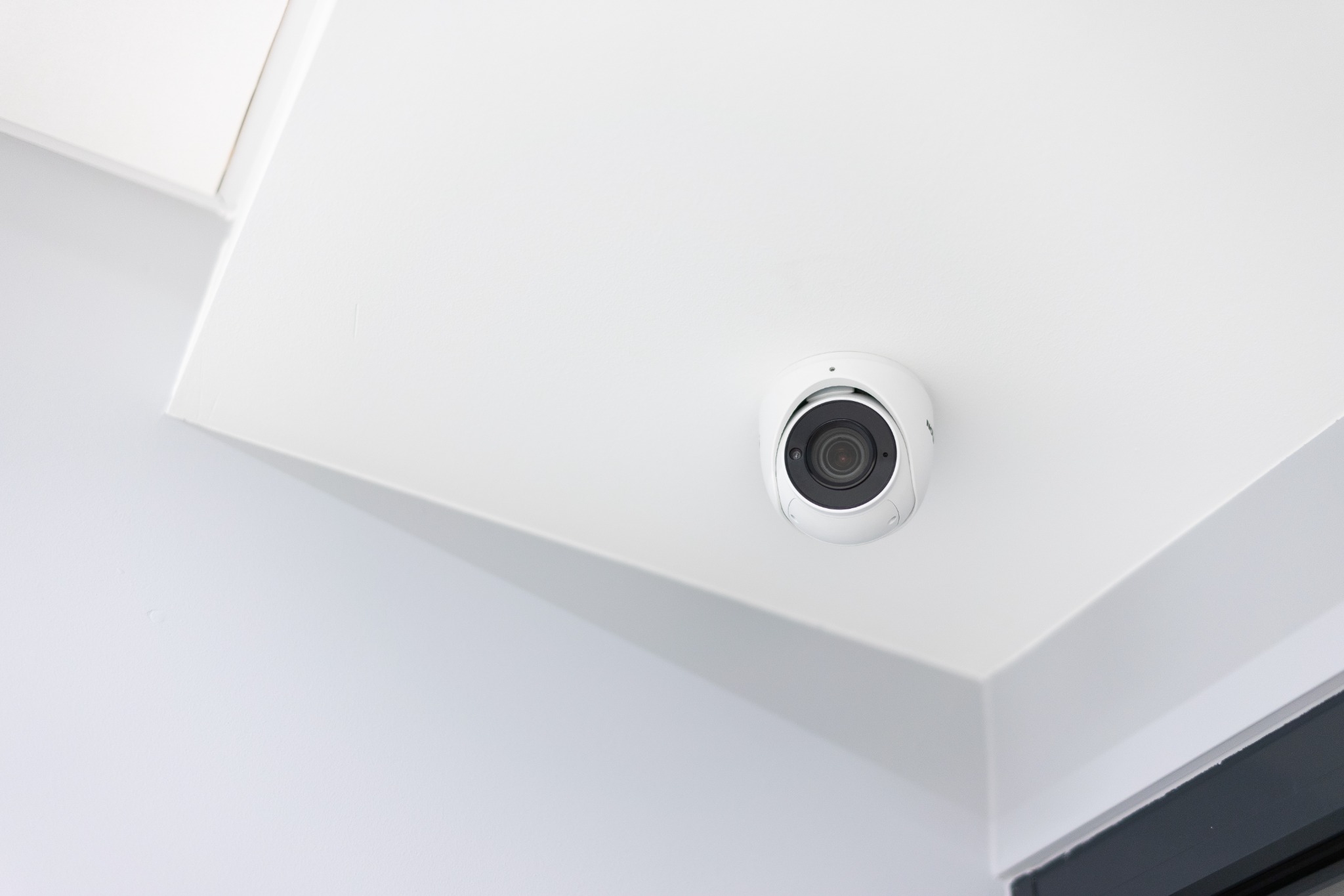 Kamera monitoringu kopułkowa, zamontowana na białym suficie w rogu pomieszczenia, widok z dołu.