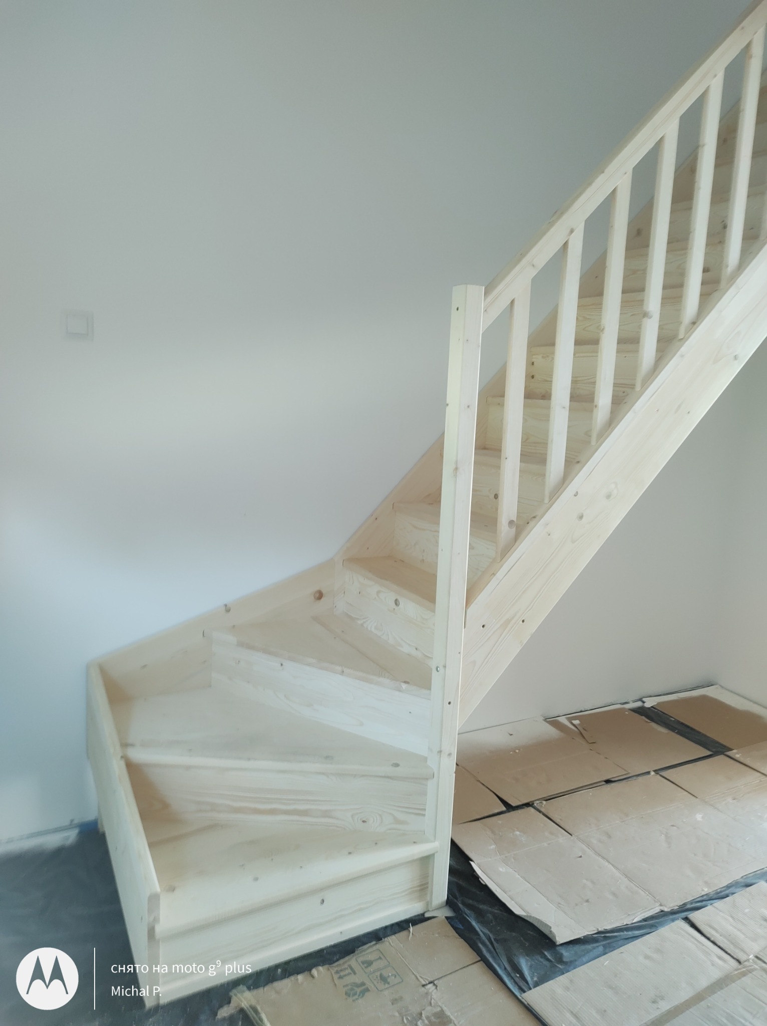 Surowe, sosnowe schody wewnętrzne z balustradą, widoczne zabezpieczenia podłogi kartonem i folią, świeżo po montażu.