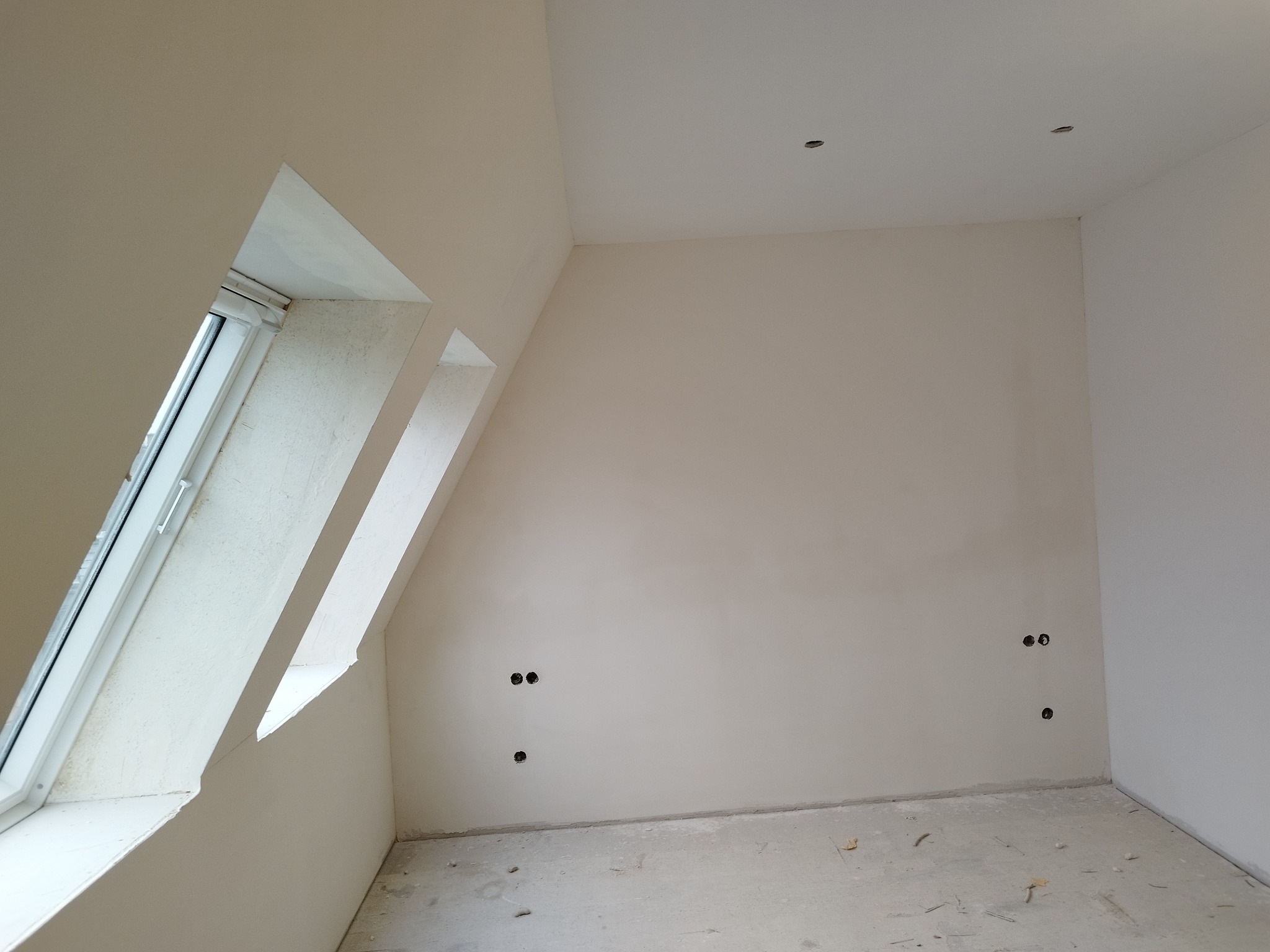 Pokój na poddaszu po szpachlowaniu ścian i sufitu, widoczne otwory pod gniazdka elektryczne i okno dachowe.