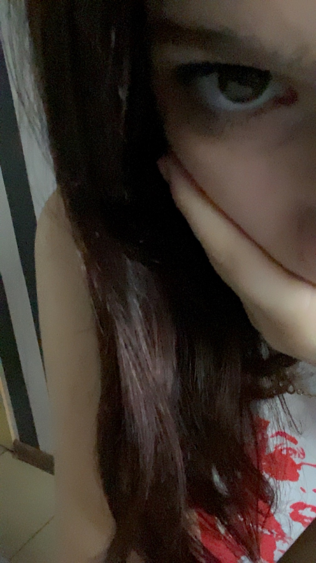 Portret kobiety z ciemnymi włosami, opierającej brodę na dłoni, z widocznym fragmentem wzorzystej koszulki i paskowanego tła.