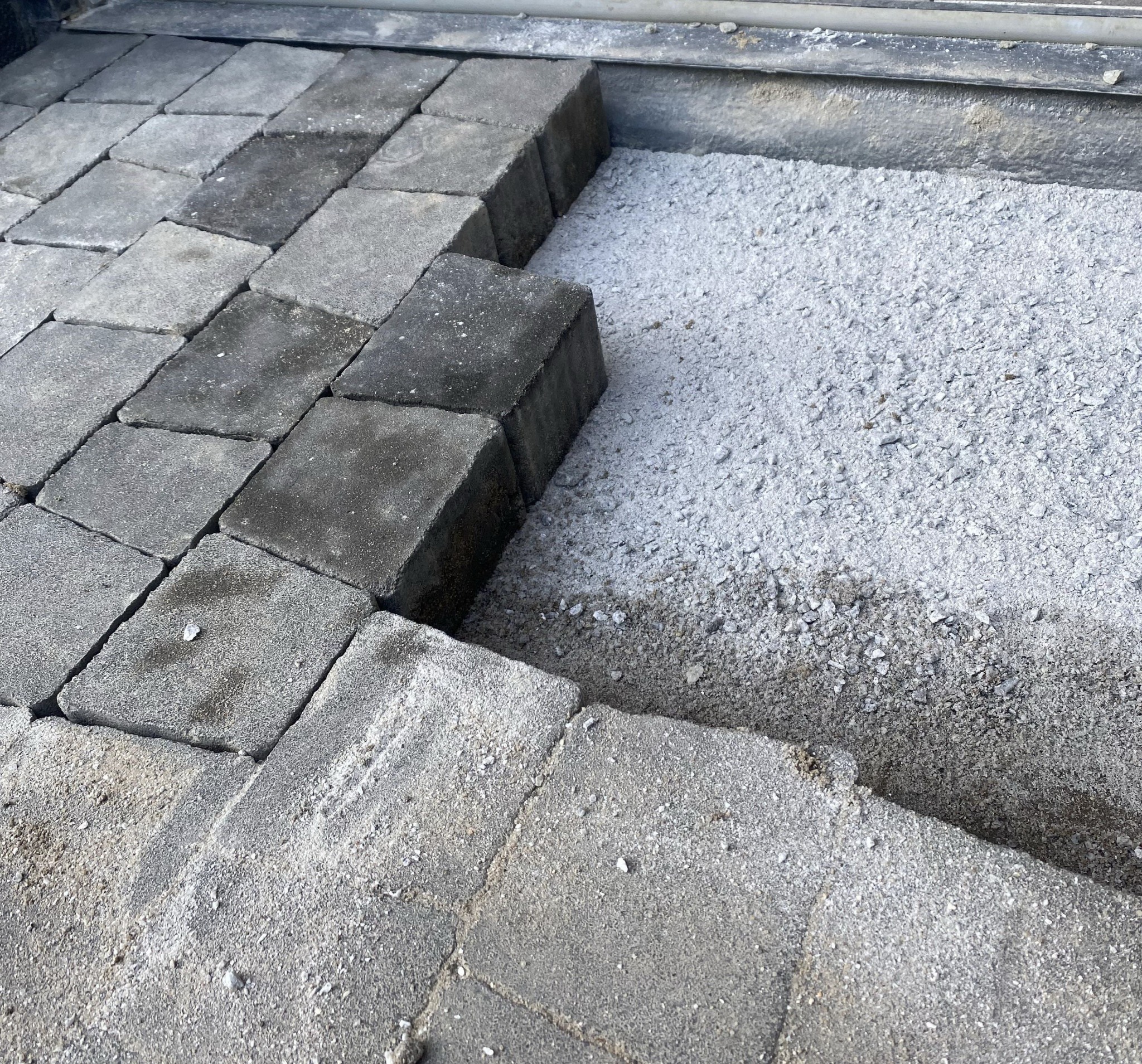 Układanie szarej kostki brukowej: widok z góry na fragment powierzchni z ułożonymi kostkami i przygotowanym podłożem z piasku.