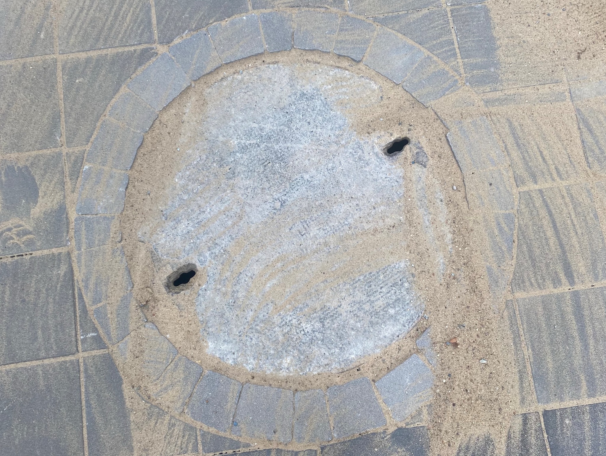 Wrocław: Szara kostka brukowa wokół okrągłego włazu kanalizacyjnego, zasypana piaskiem.