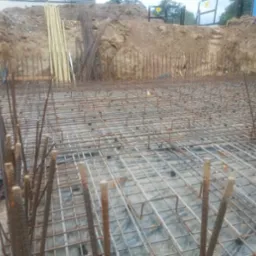 Siatka zbrojeniowa przygotowana pod fundamenty budynku we Wrocławiu, widoczne wystające pręty, folia izolacyjna i wykop ziemny w tle.