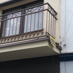 GSM SPOLKA Z OGRANICZONA ODPOWIEDZIALNOSCIA - Kuty balkon z ozdobnymi elementami i żółtą tabliczką ostrzegawczą przymocowaną do barierki, widok z dołu.