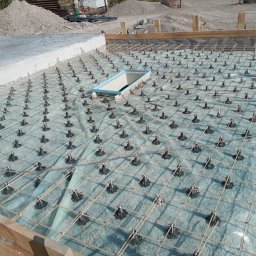 GSM SPOLKA Z OGRANICZONA ODPOWIEDZIALNOSCIA - Przygotowanie zbrojenia płyty fundamentowej z użyciem dystansów pod siatką, widoczny szalunek i wykop pod studzienkę rewizyjną.