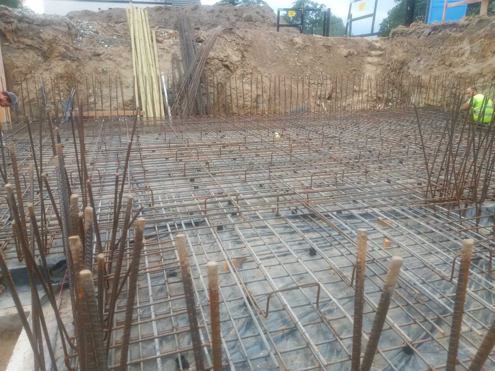 Siatka zbrojeniowa przygotowana pod fundamenty budynku we Wrocławiu, widoczne wystające pręty, folia izolacyjna i wykop ziemny w tle.