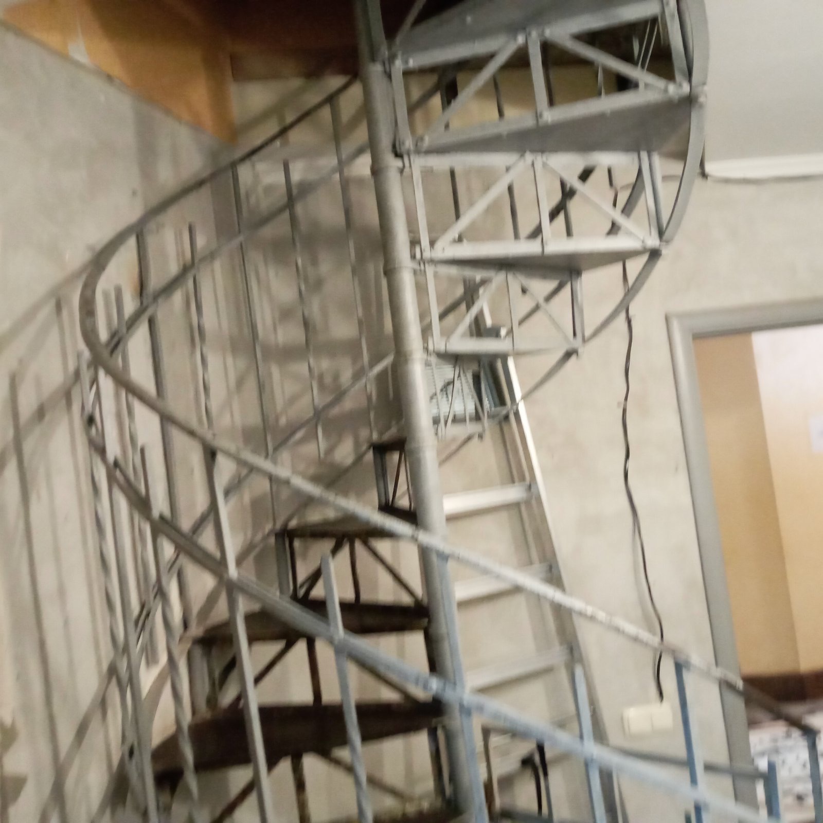 Metalowe schody spiralne z widoczną konstrukcją nośną, prowadzące na wyższą kondygnację budynku, surowe wykończenie ścian.