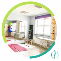 Jasne wnętrze gabinetu rehabilitacyjnego z drabinkami, leżankami, piłkami do ćwiczeń i lustrem odbijającym wyposażenie