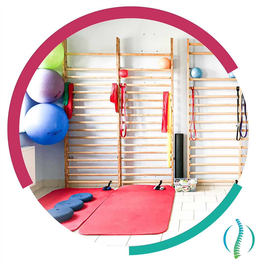 Sala rehabilitacyjna z drabinkami gimnastycznymi, matami, piłkami do ćwiczeń i akcesoriami, widok z perspektywy pacjenta.
