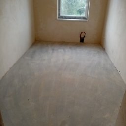 Jarosław Majchrowicz - Pokój po wylewce podłogi, ściany przygotowane pod malowanie, widoczne rury instalacji grzewczej przy oknie.