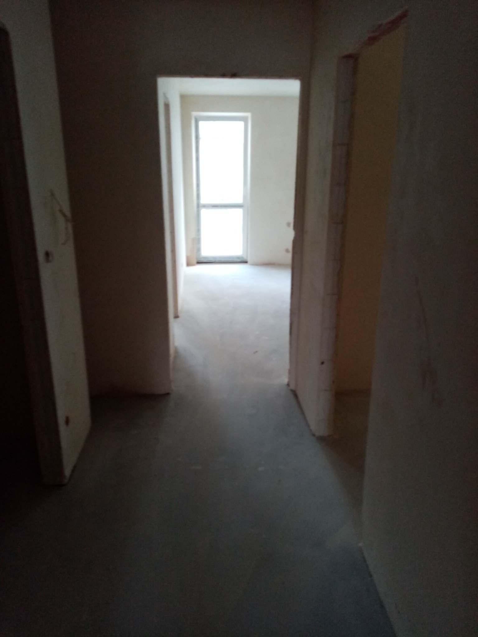 Wnętrze mieszkania w trakcie prac wykończeniowych, widoczne surowe ściany przygotowane do dalszych prac, w tle okno z dostępem światła dziennego.