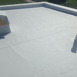 L.W.Hall Łukasz Wójcik - Nowo położona, jasnoszara membrana dachowa na płaskim dachu z widocznymi detalami, takimi jak kominek wentylacyjny zabezpieczony taśmą i rura odpowietrzająca.