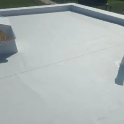 Nowo położona, jasnoszara membrana dachowa na płaskim dachu z widocznymi detalami, takimi jak kominek wentylacyjny zabezpieczony taśmą i rura odpowietrzająca.