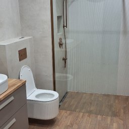 Kar-Bud - Nowoczesna łazienka z kabiną prysznicową typu walk-in, drewnopodobną podłogą i wiszącą toaletą. Armatura w kolorze miedzi dodaje elegancji.