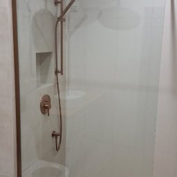 Kar-Bud - Nowoczesna kabina prysznicowa walk-in z armaturą w kolorze miedzi, wykończona drewnopodobnymi płytkami podłogowymi. Minimalistyczny design, jasne płytki ścienne.