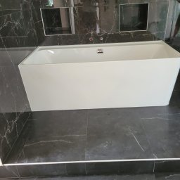 Kar-Bud - Nowoczesna, prostokątna wanna w łazience wyłożonej czarnym marmurem z białymi żyłami; w tle widać lustro i wnęki w ścianie.