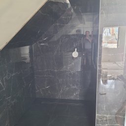 Kar-Bud - Wykończona kabina prysznicowa w łazience na poddaszu, wyłożona czarnymi płytkami imitującymi marmur z widocznym odpływem liniowym i zamontowaną baterią Grohe; w lustrzanej powierzchni odbija się...