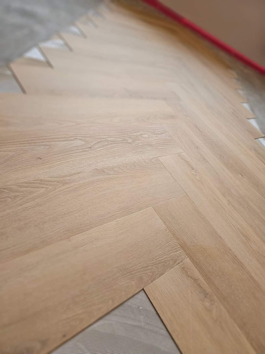 Układanie jasnego parkietu w jodełkę francuską, widoczne docięte elementy i podłoże pod parkiet.