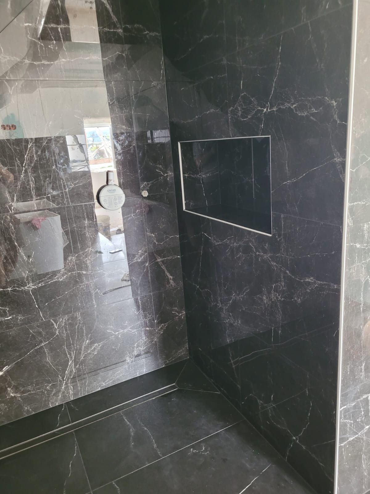 Wykończona kabina prysznicowa w Oleśnicy z czarnymi płytkami imitującymi marmur, wbudowana półka w ścianie, widoczna bateria Grohe.