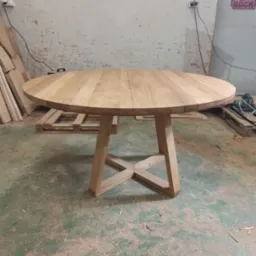 Okrągły, rozkładany stół z jasnego drewna z charakterystyczną podstawą w kształcie litery X, widoczny w warsztacie z surowym tłem i plakatem 'Rock'.