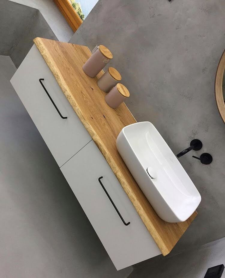 Nowoczesna łazienka: biała szafka z drewnianym blatem, na którym ustawiono ceramiczną umywalkę i trzy dekoracyjne pojemniki z drewnianymi pokrywkami; czarne, minimalistyczne uchwyty i bateria.