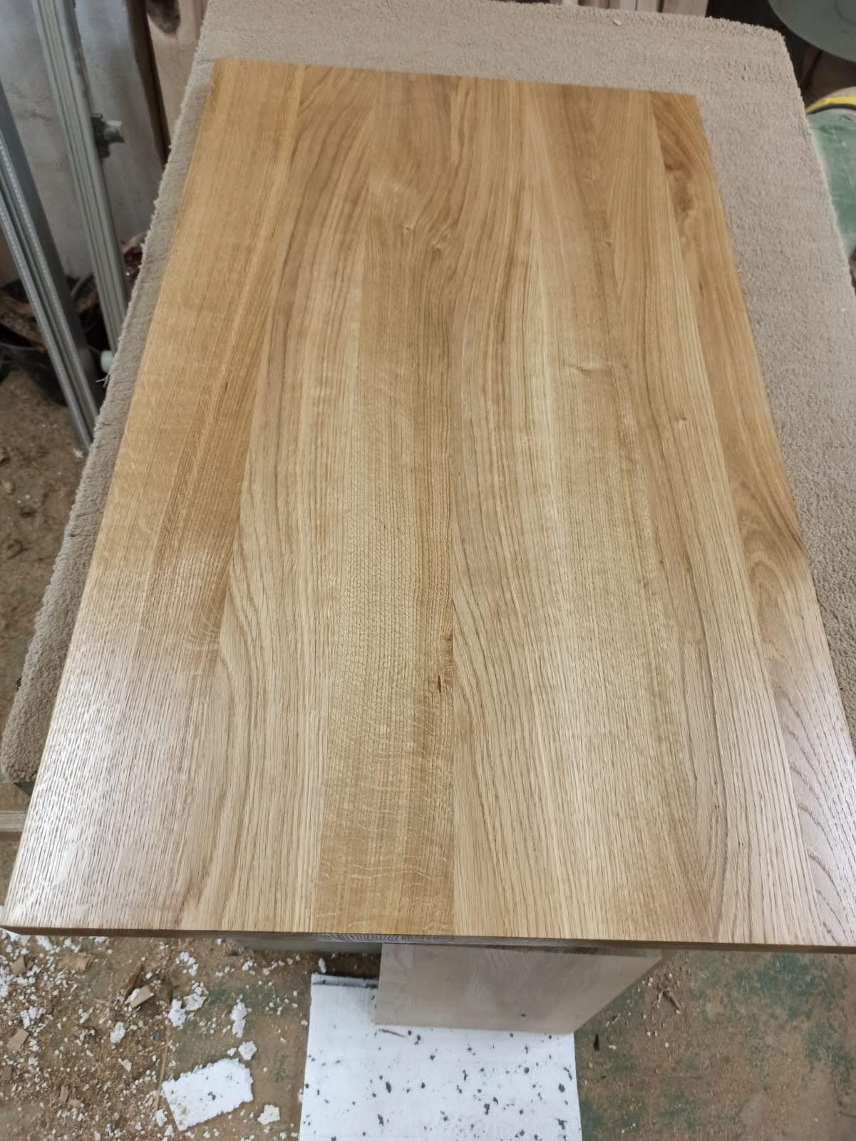 Blat z jasnego drewna dębowego, widoczne naturalne słoje i tekstura drewna, na stole roboczym w warsztacie.