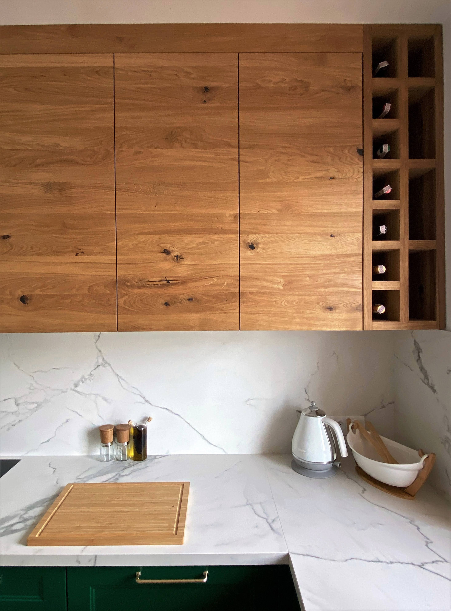 Kuchnia z drewnianymi szafkami górnymi z wbudowanym regałem na wino, blatem z białego marmuru i zielonymi szafkami dolnymi.