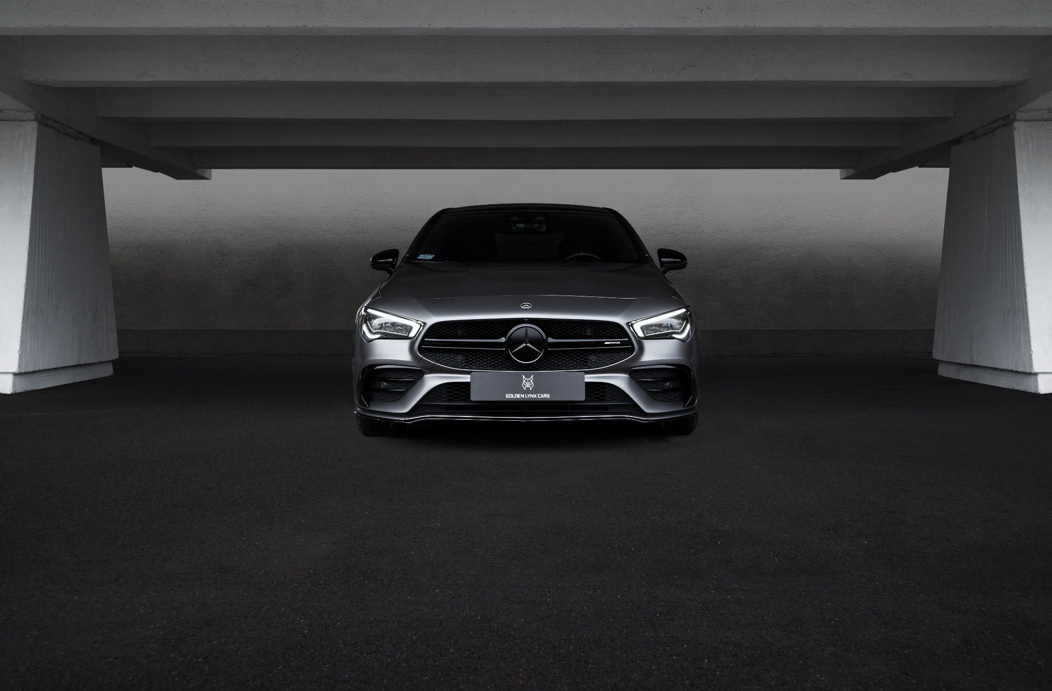 Szary Mercedes AMG zaparkowany w betonowym garażu, widok z przodu, z włączonymi światłami, tablica z logo Golden Lynx Cars.