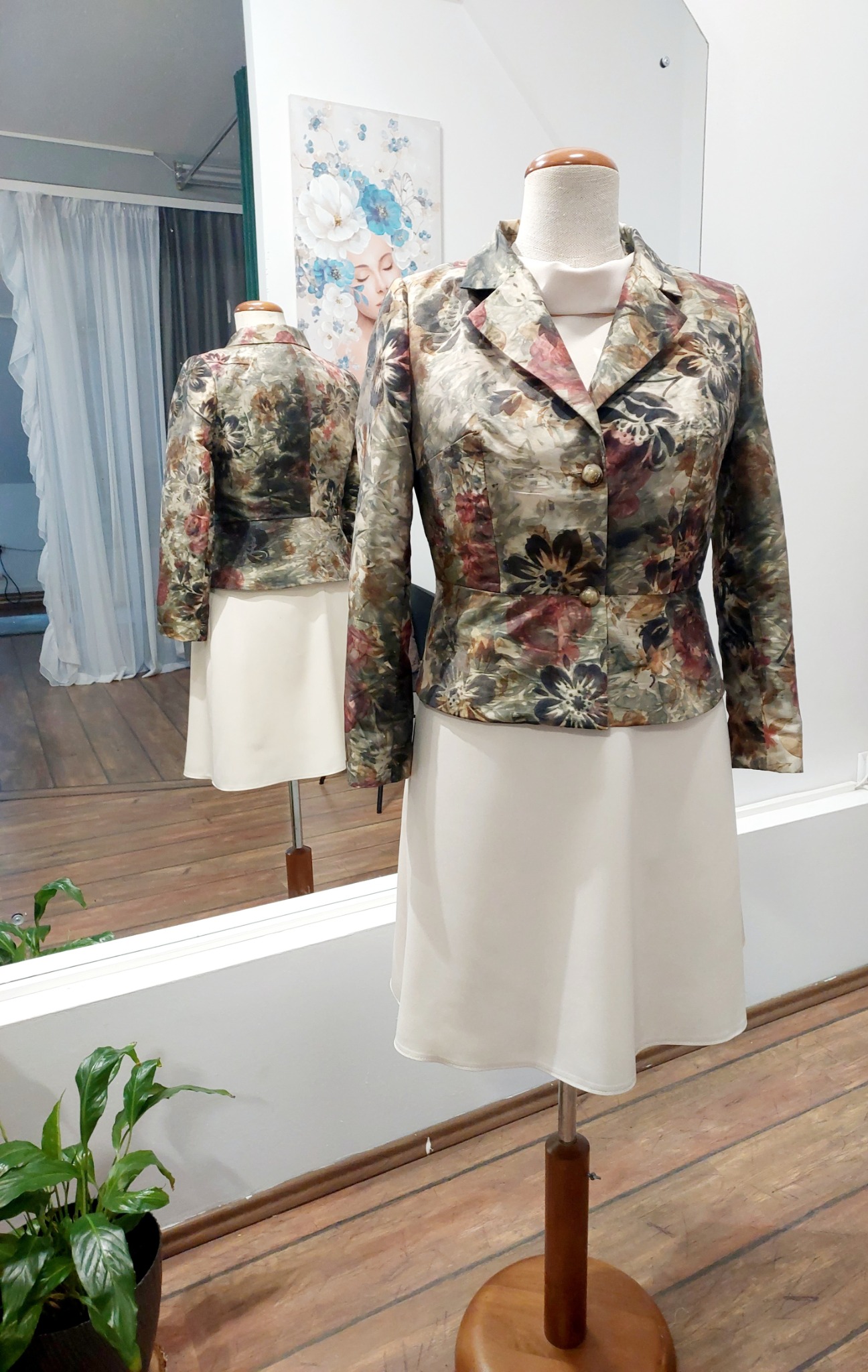 Żakiet damski w kwiatowy wzór i kremowa spódnica na manekinie, z odbiciem w lustrze i rośliną w tle.