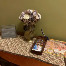 Aranżacja biurowa na drewnianym biurku z kwiatami w metalowym wazonie, metalowym organizerem na dokumenty, wiklinowym koszykiem z wizytówkami i kolorową mapą świata.