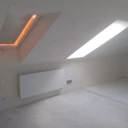 ABRemonty - Poddasze po nałożeniu gładzi, widoczne dwa okna dachowe - jedno z pomarańczową poświatą, drugie z białym światłem dziennym, grzejnik na ścianie.