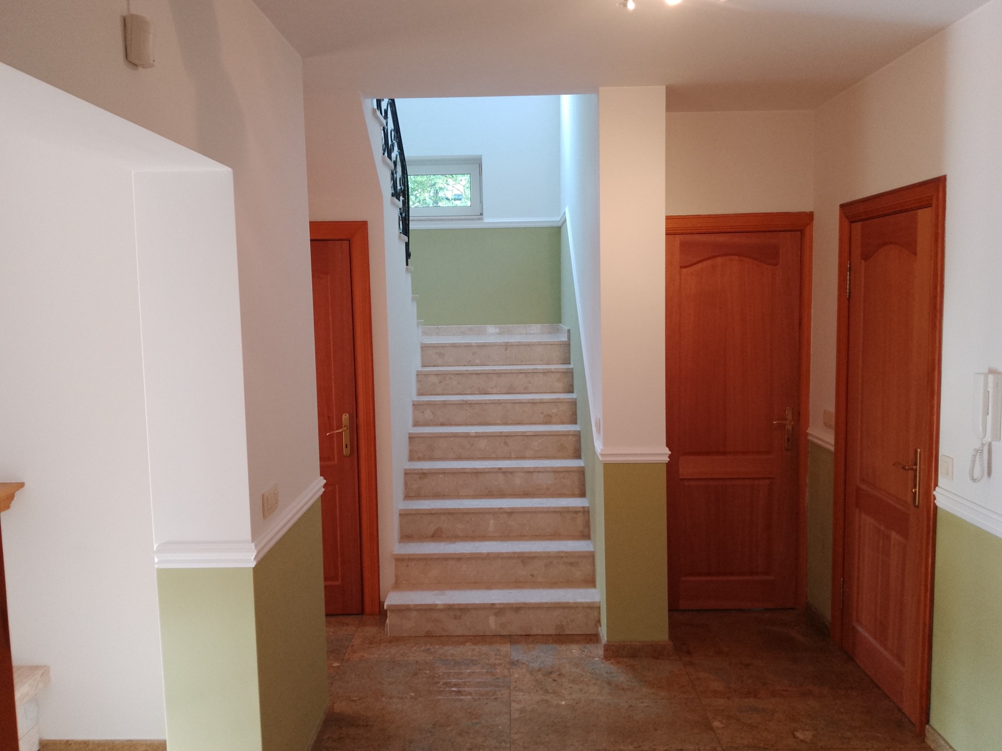 Korytarz z marmurowymi schodami, pomalowanymi na biało ścianami z zielonym akcentem u dołu i drewnianymi drzwiami po bokach.