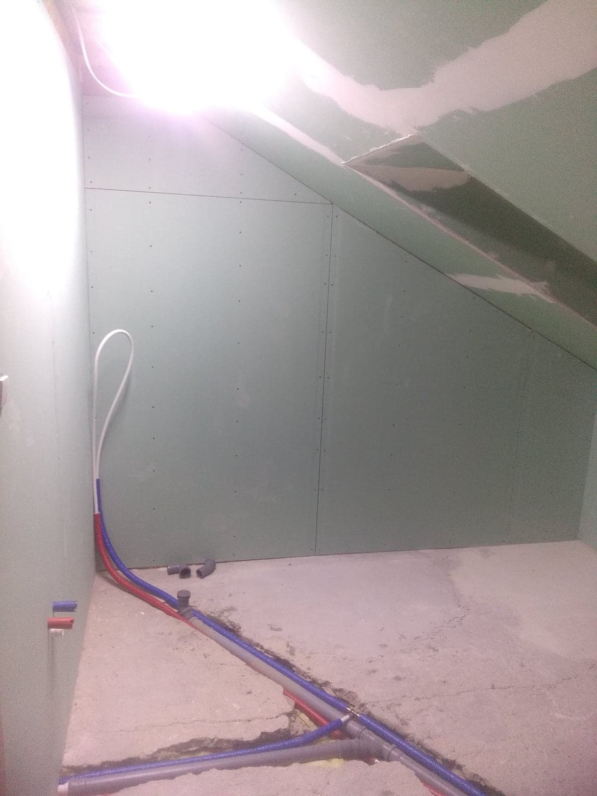 Poddasze z płytami gipsowo-kartonowymi na ścianach i suficie, widoczne rury instalacji wodnej i kanalizacyjnej w podłodze przed dalszymi pracami wykończeniowymi.