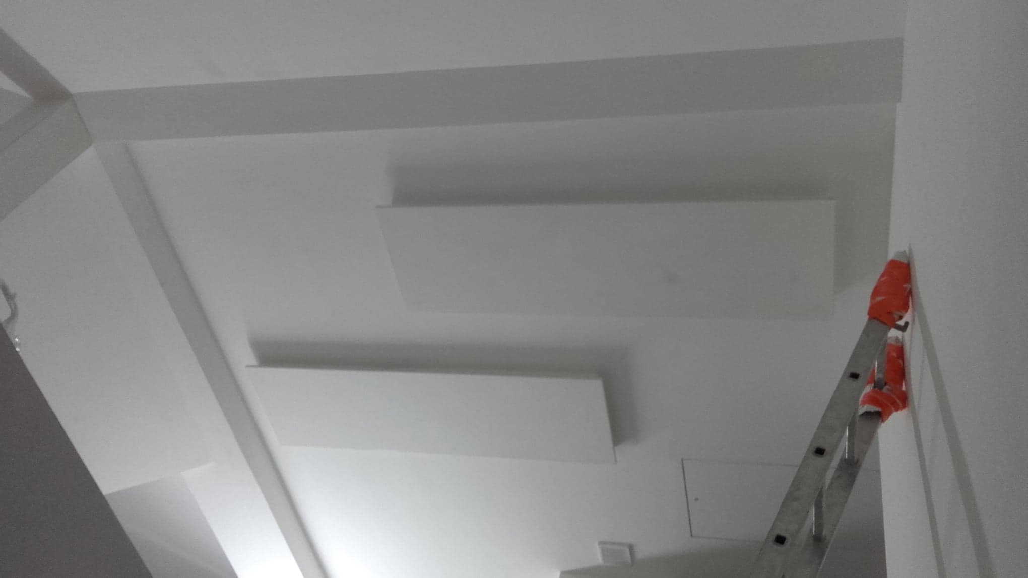 Białe, świeżo pomalowane sufity z ozdobnymi listwami, widoczna drabina z zabezpieczeniem na ścianie.