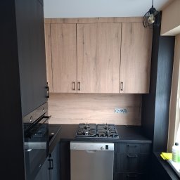 HR-Home Łukasz Ślusarek - Nowoczesna kuchnia na wymiar z czarnymi frontami i drewnianymi szafkami wiszącymi. Widoczna płyta gazowa i zintegrowana z zabudową zmywarka Bosch.